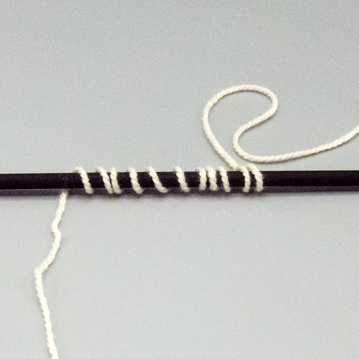White DK weight yarn wrapped around a black stick.