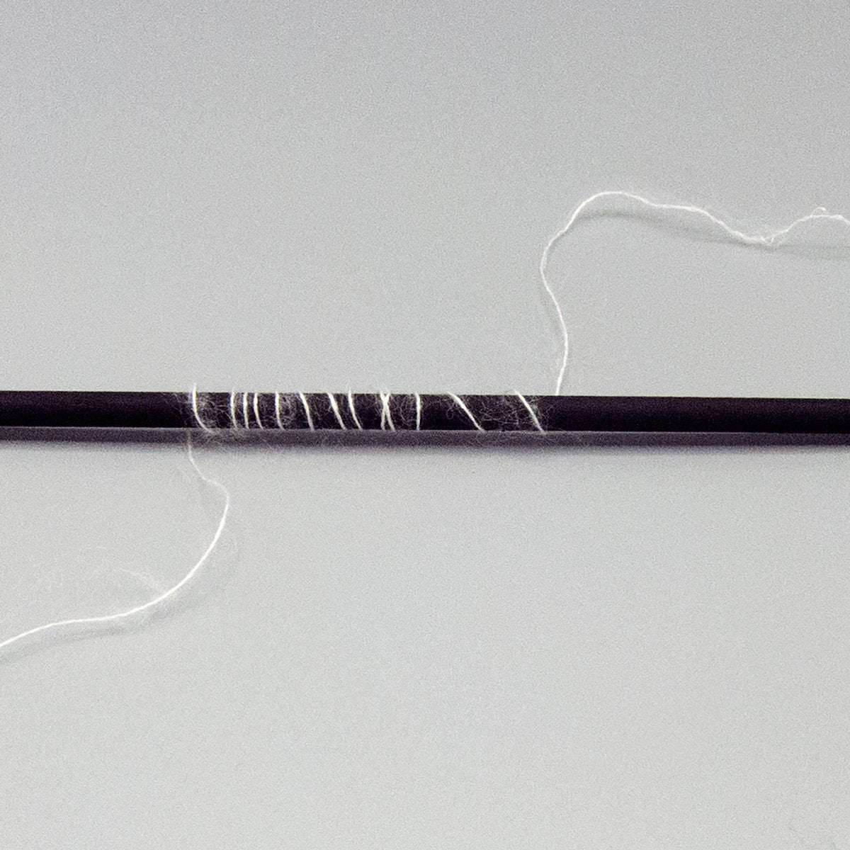 White lace weight yarn wrapped around a black stick