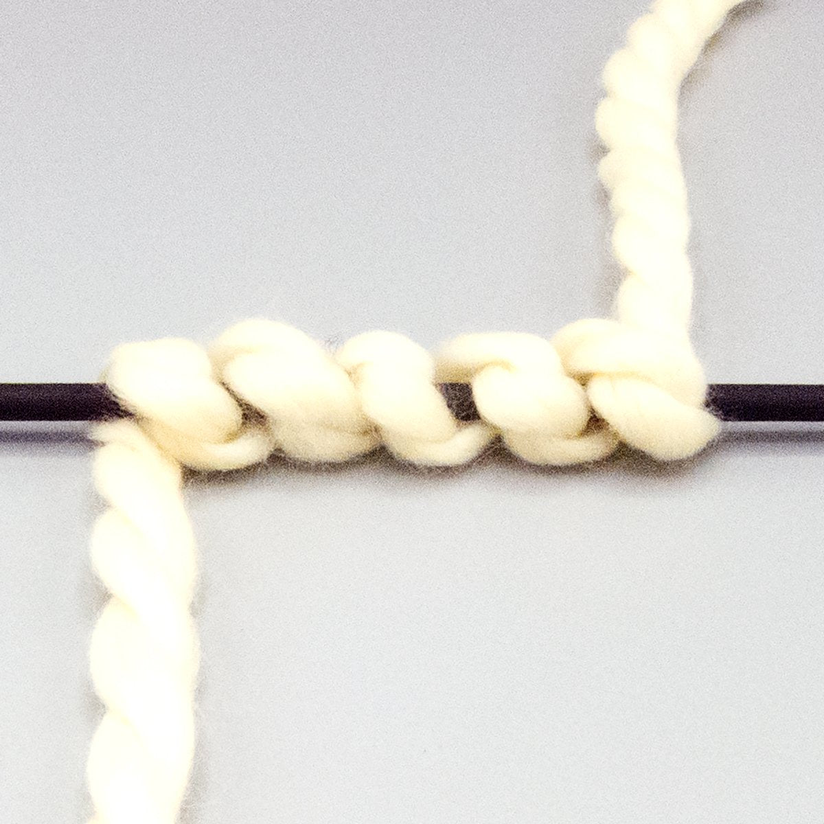 Off white bulky yarn wrapped around a black stick