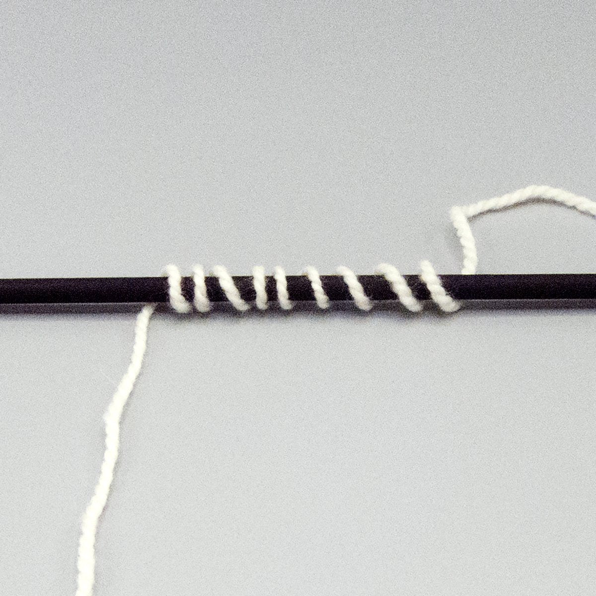 White worsted weight yarn wrapped around a black stick.