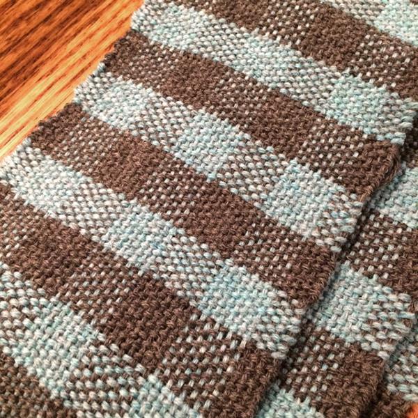 A grey and blue hand woven scarf in a checkerboard pattern.  