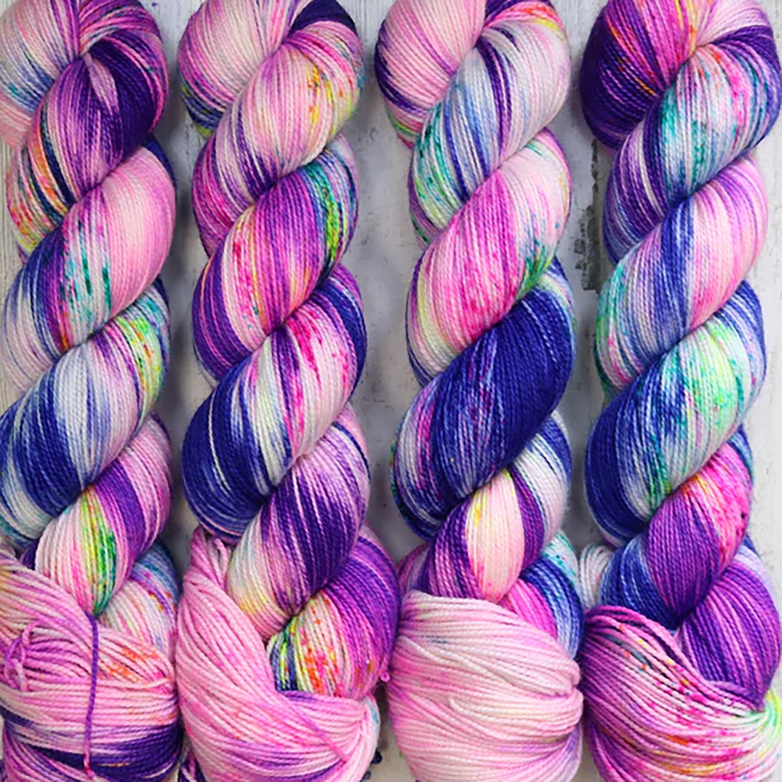 Four skeins of Northwood Fibers Butternut Sock in Amped, a variegated dark purple, light pink, neon pink, 