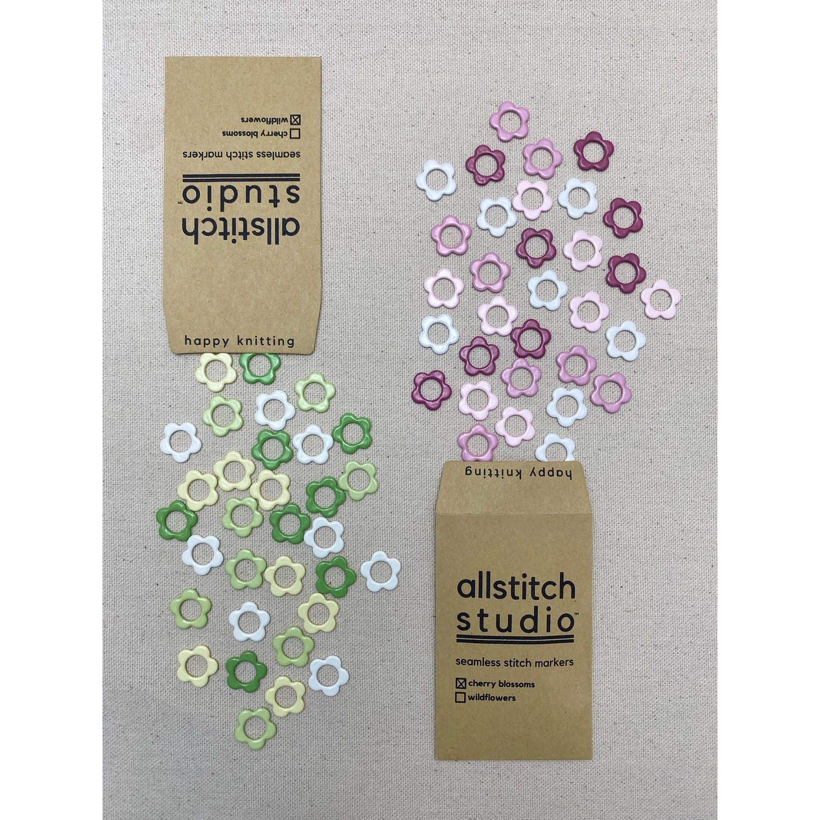 A packet of wildflower stitch markers in green and white, and a packet of cherry stitch markers in pink and white