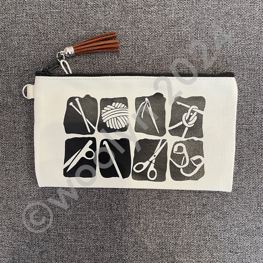 Image of a white canvas zip pouch with a tassel zipper and black blocky graphic illustrations of fiber craft tools.