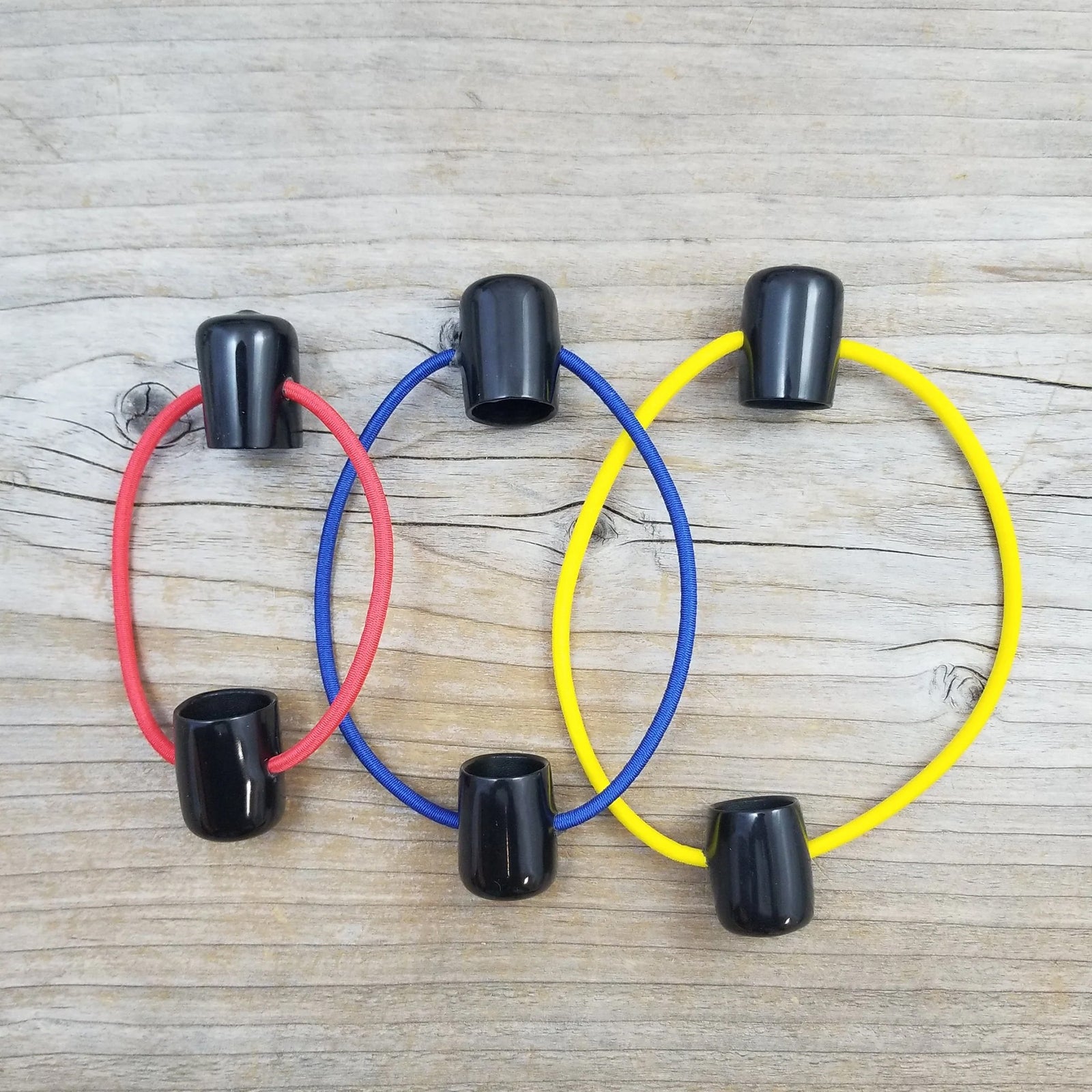A photo of three different sizes of elastic DPN holders with black end caps; small with red bands, medium with blue bands, and large with yellow bands