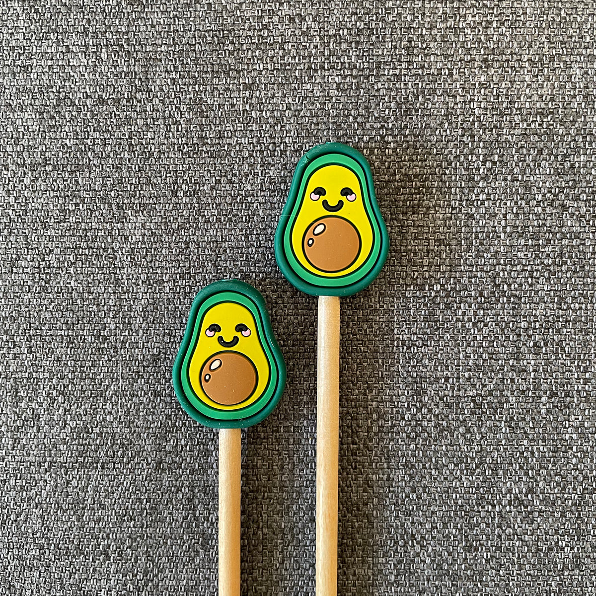 Two knitting needles topped with smiling avocado Stitch Stoppers
