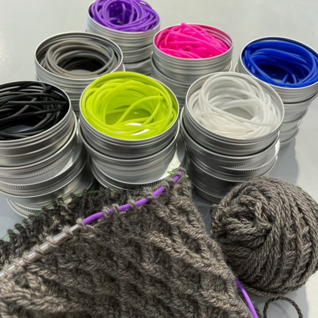 Tins of Purl Strings in various colors including neon yellow, neon pink, white, black, grey, bright purple and blue.  Along with bright purple purl strings at work on a cable project.