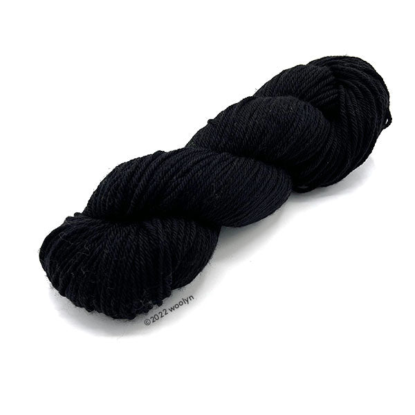 A skein of Knitted Wit Worsted Superwash in Guy Noir a solid black color.