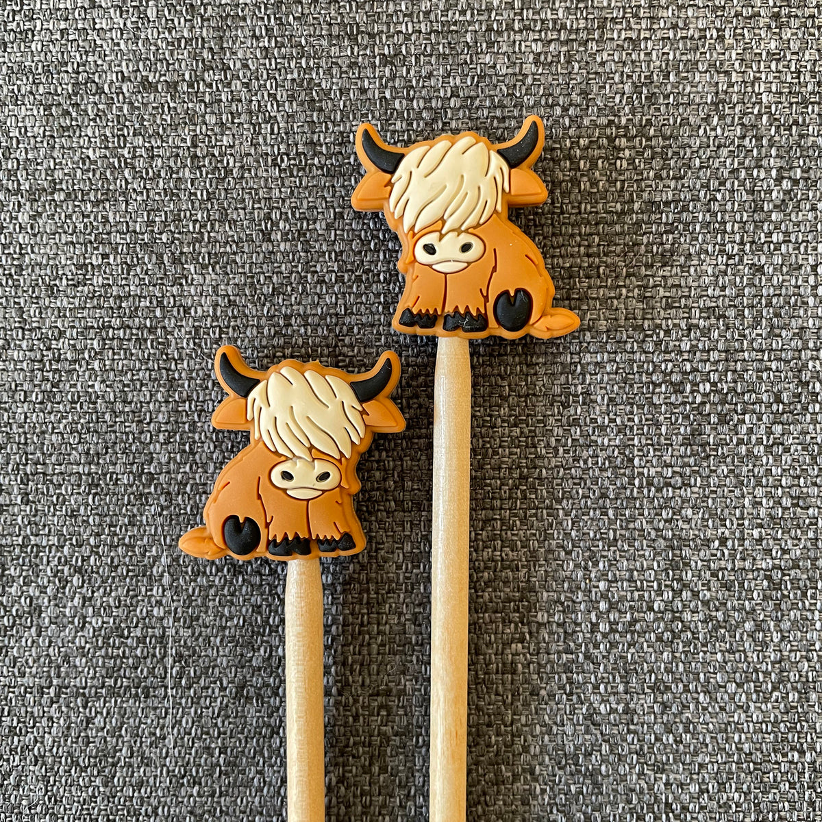 Two knitting needles topped with Highland Cow Stitch Stoppers