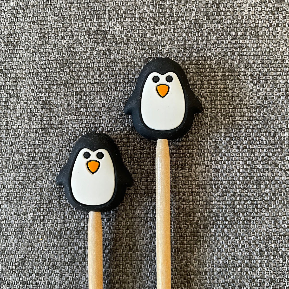 Two knitting needles topped with penguin Stitch Stoppers