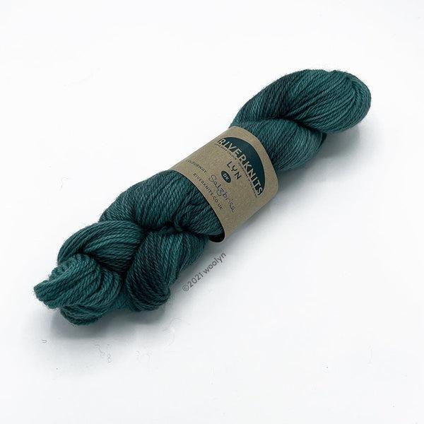 A skein of River Knits Lyn a worsted plied DK weight yarn in Salzbrise, a turquoise color with dark teal undertones.