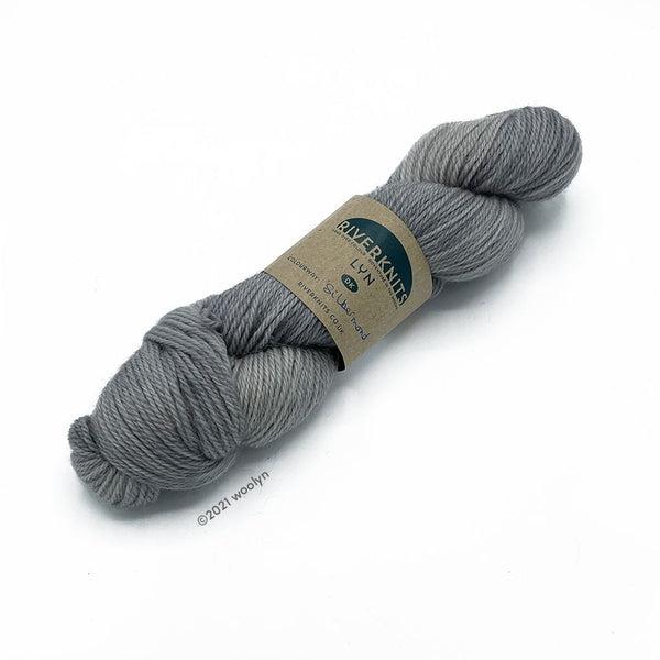 A skein of River Knits Lyn a worsted plied DK weight yarn in Sibermond, a pale grey color.