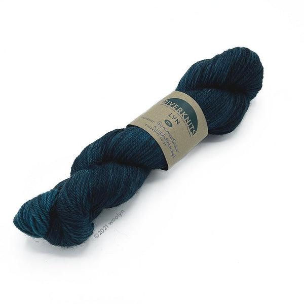 A skein of River Knits Lyn a worsted plied DK weight yarn in Sommerlicher Nachthimmel, a dark teal color.