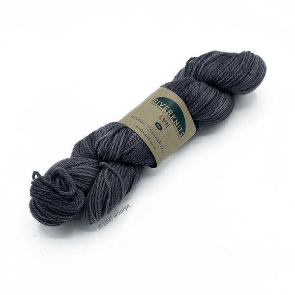 A skein of River Knits Lyn a worsted plied DK weight yarn in Steinchen, a medium grey color.