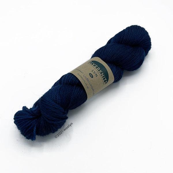 A skein of River Knits Lyn a worsted plied DK weight yarn in Unterwasswerwelt, a dark royal blue color.