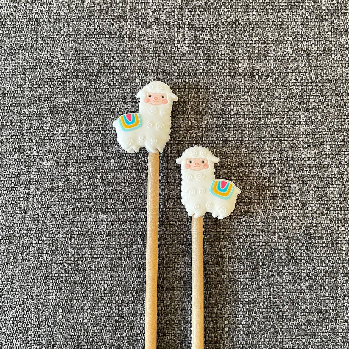 Two knitting needles topped with Llama Stitch stoppers arranged in