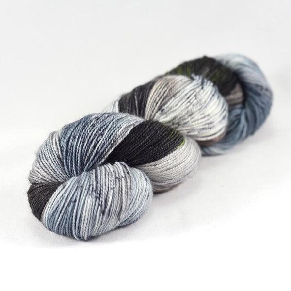 Skein of Destination Yarn Passport Eliean Donan Castle, a variegated and speckled yarn in several shades of grey and dark brown with blue undertones. 