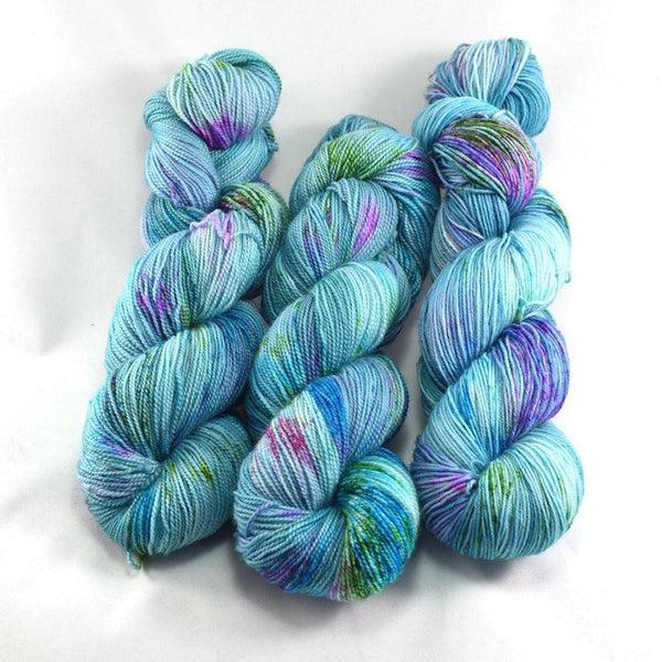 Skeins of Destination Yarn Passport Swim Up Bar, a bright, light tonal turquoise with small random sections of purple, pink and bright green. 