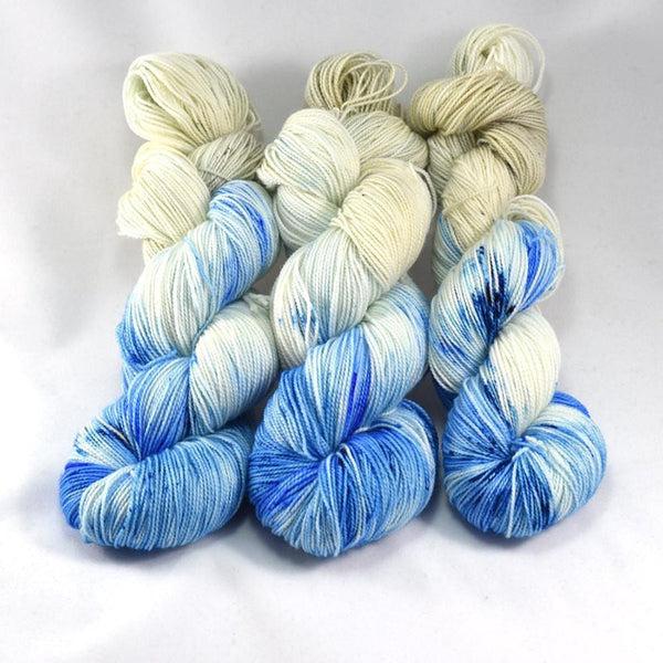 Skeins of Destination Yarn Passport Toes in the Sand, a variegated yarn in shades of sand, white and bright blue with small sections of dark blue.  