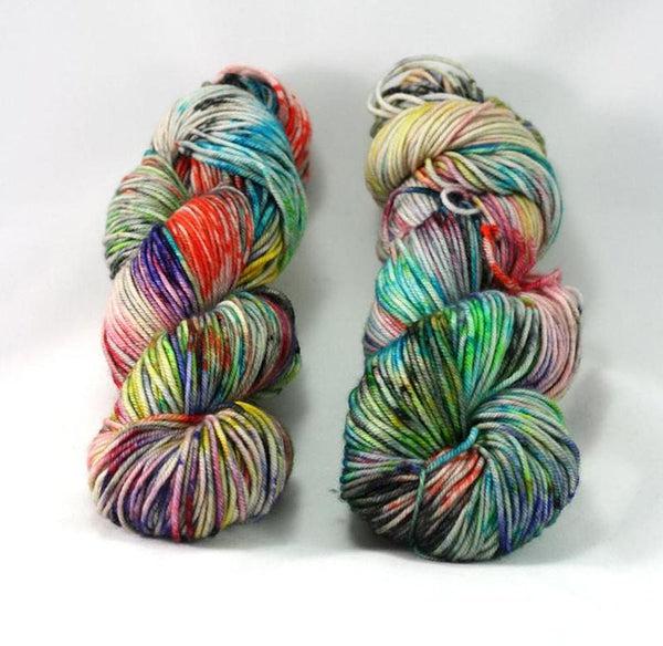 Skeins of Destination Yarn Souvenir Color Run, a highly variegated and speckled skein in many shades of yellow, orange, purple, green and pink. 