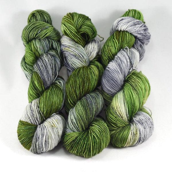 Skeins of Destination Yarn Souvenir Glen Coe, a variegated yard in tonal shades of light and medium grey with light and medium green.  
