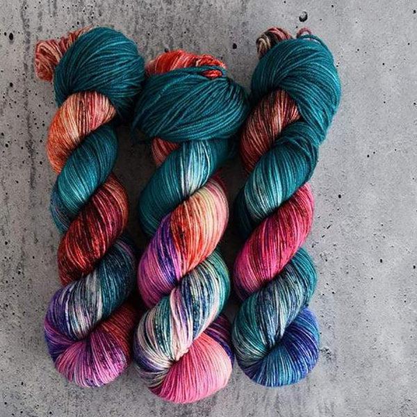 Skeins of Destination Yarn Souvenir Honolulu, a variegated and speckled yarn with deep teal, cobalt blue, oranges, purples and pinks. 