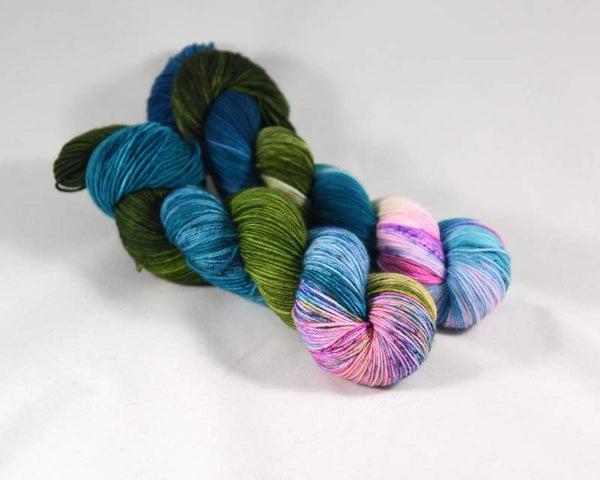 Skeins of Destination Yarn Souvenir Kauai, a brightly variegated yarn in shades of medium and light blue with dark green and bright, light pink and turquoise. 