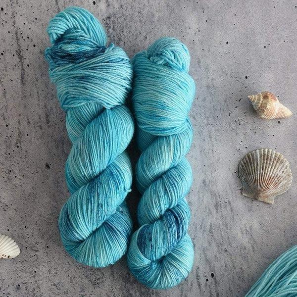 Skeins of Destination Yarn Souvenir Lagoon, a bright, light tonal turquoise blue with darker blue speckles. 