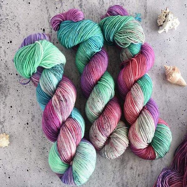 Skeins of Destination Yarn Souvenir Maui, a brightly variegated yarn in shades of seafoam green, sand, orchid pink, coral, and light purple. 
