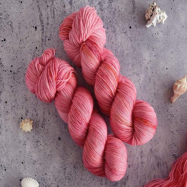 Skeins of Destination Yarn Souvenir Plumeria, a bright pink with hits of darker pink and crimson. 