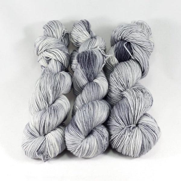 Skeins of Destination Yarn Souvenir Standing Stones, a variegated and speckled yarn in shades of pale and medium grey with minimal spots of darker grey.