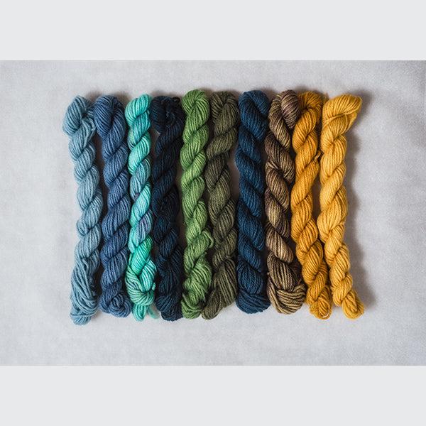 10 mini skeins of Jade Sapphire Coloring Box Trail Mix-and pattern booklet in deep earth tones of yellow, teal, blue and green.