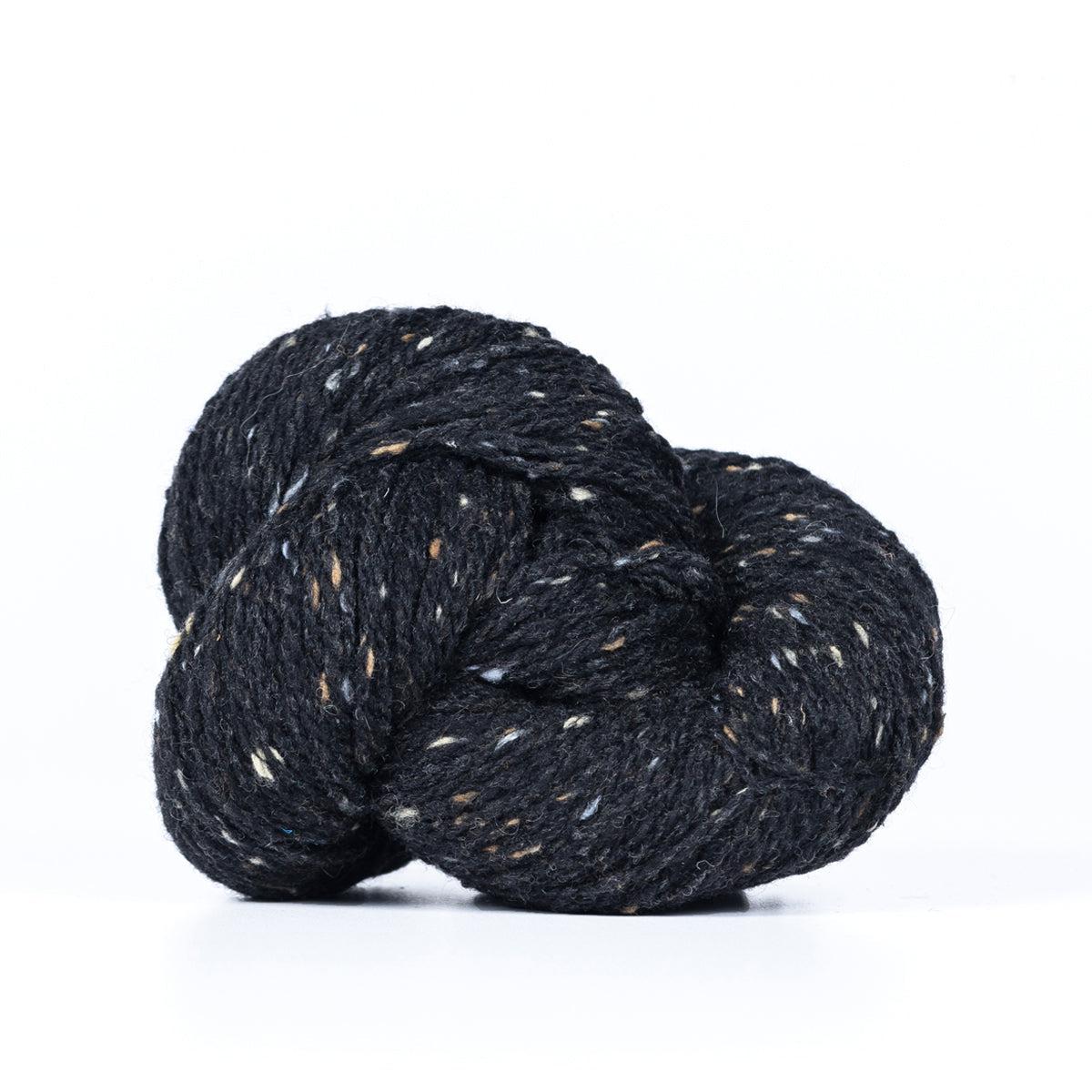 A skein of Kelbourne Woolens Lucky Tweed Black, a black tweed with cream, light brown and grey.