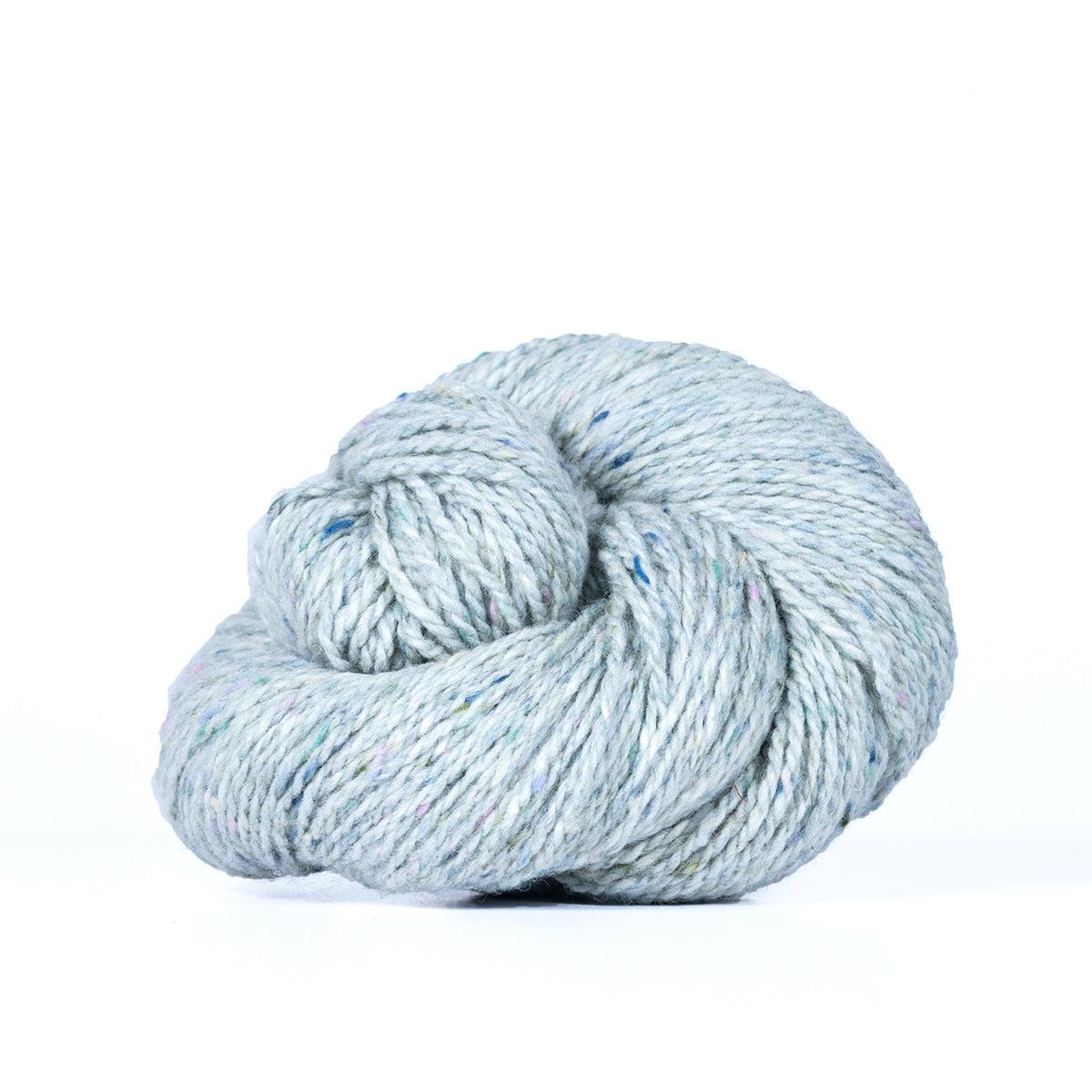 A skein of Kelbourne Woolens Lucky Tweed Fog, a bright light blue grey with white and darker blue flecks.