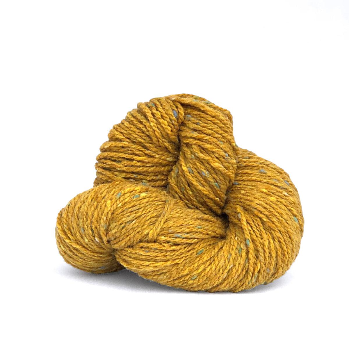 A skein of Kelbourne Woolens Lucky Tweed Golden, a mustard yellow with green and blue flecks.