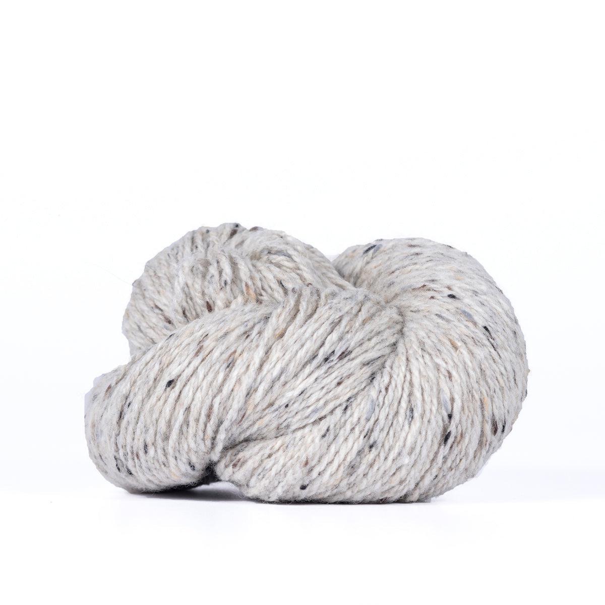 A skein of Kelbourne Woolens Lucky Tweed Light Grey, a light grey with darker brown and grey flecks.