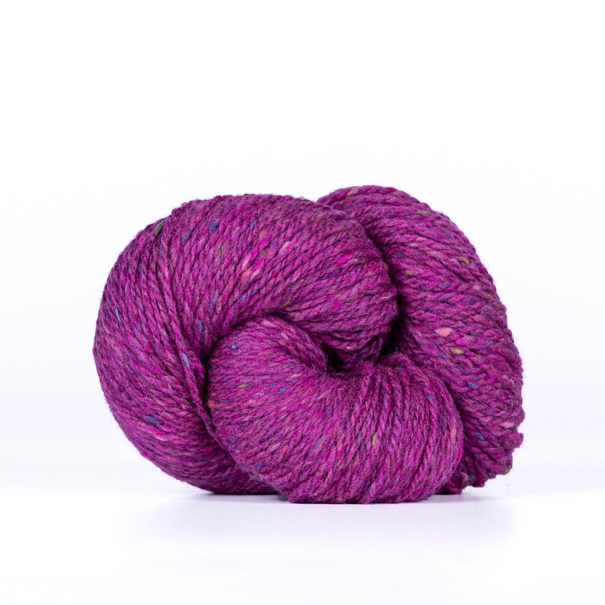 A skein of Kelbourne Woolens Lucky Tweed Magenta, a bright pink purple with pink, blue and yellow flecks.