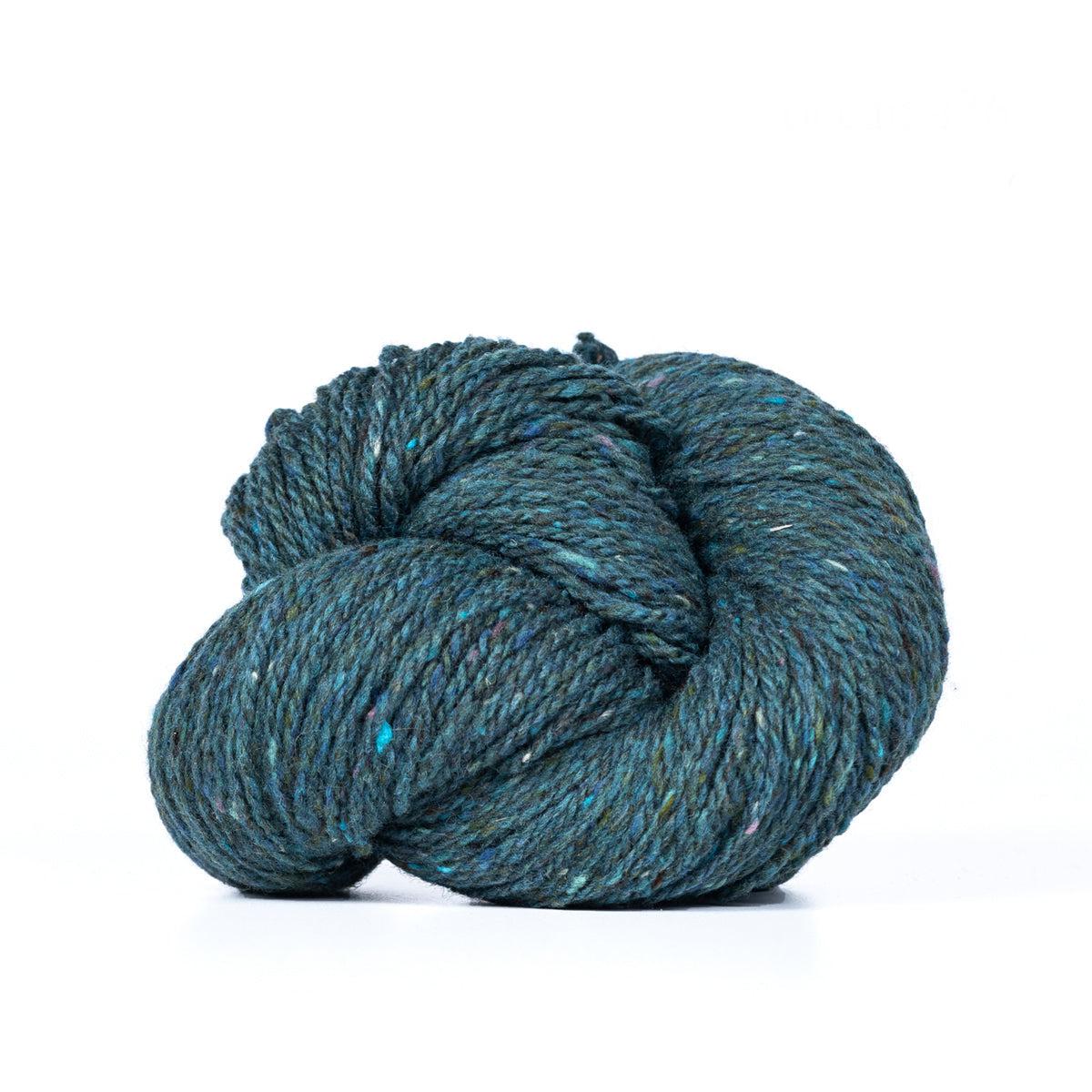 A skein of Kelbourne Woolens Lucky Tweed Ocean, a dark teal with brighter blue and grey flecks.