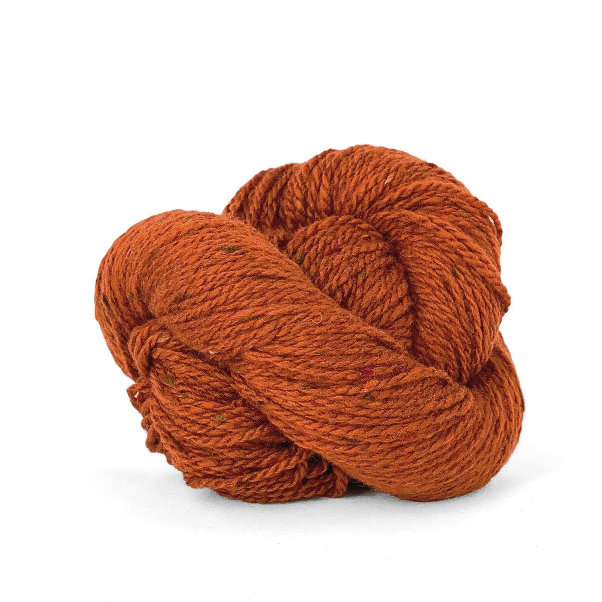 A skein of Kelbourne Woolens Lucky Tweed Orange Spice, a dark pumpkin orange with brown and green flecks.