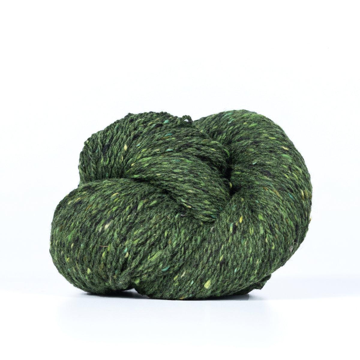 A skein of Kelbourne Woolens Lucky Tweed Pine, a dark green with lighter green and yellow flecks.