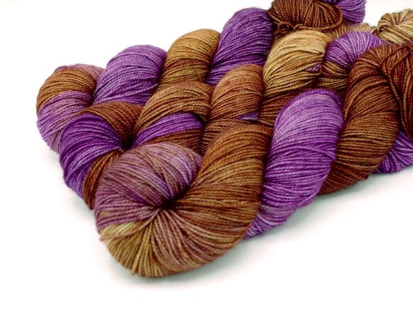 Skeins of Murky Depths Deep Sock Caravanasary, a variegated yarn in shades of purple, light and dark golden brown.