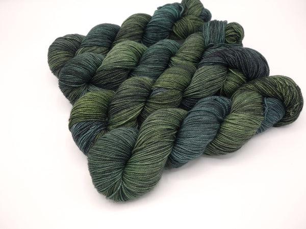 Skeins of Murky Depths Deep Sock No More Shall We Part, a gently variegated yarn in tonal shades of dark green and blue with grey overtones.