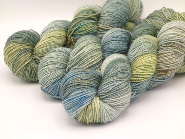Skeins of Murky Depths Deep Sock Water Babies, a variegated yarn with pale yellows, blues and greens. 
