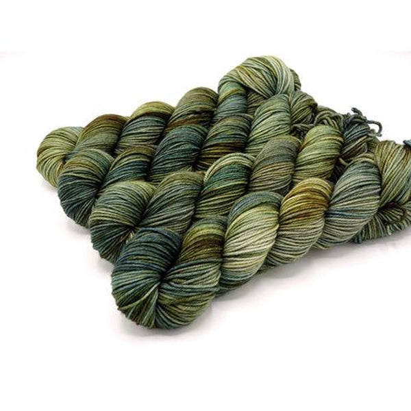 Skeins of Murky Depths Neptune DK Brackish, a variegated yarn in shades of green ranging from light grey green to a deep evergreen. 