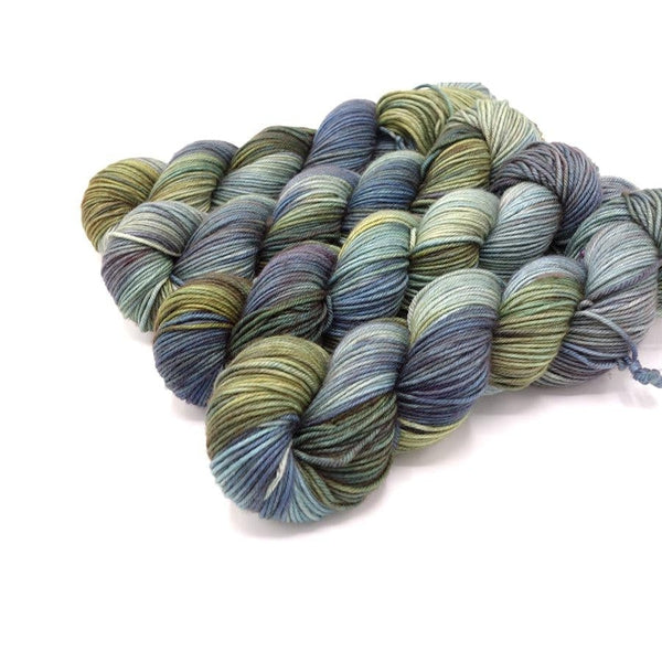 Skeins of Murky Depths Neptune DK Fast Eddy, a variegated yarn in shades of light grey blue, deeper navy, pale and army greens. 