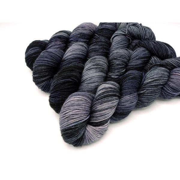 Skeins of Murky Depths Neptune DK Ghost Rider, a variegated yarn in shades of grey with a purple tone. 