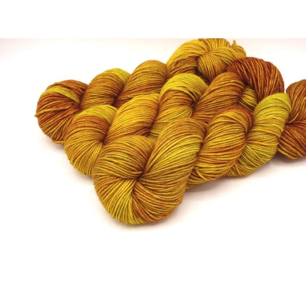Skeins of Murky Depths Neptune DK Mysore Silk, a tonally variegated yarn in shades of golden yellow, and orange with slight brown tones. 