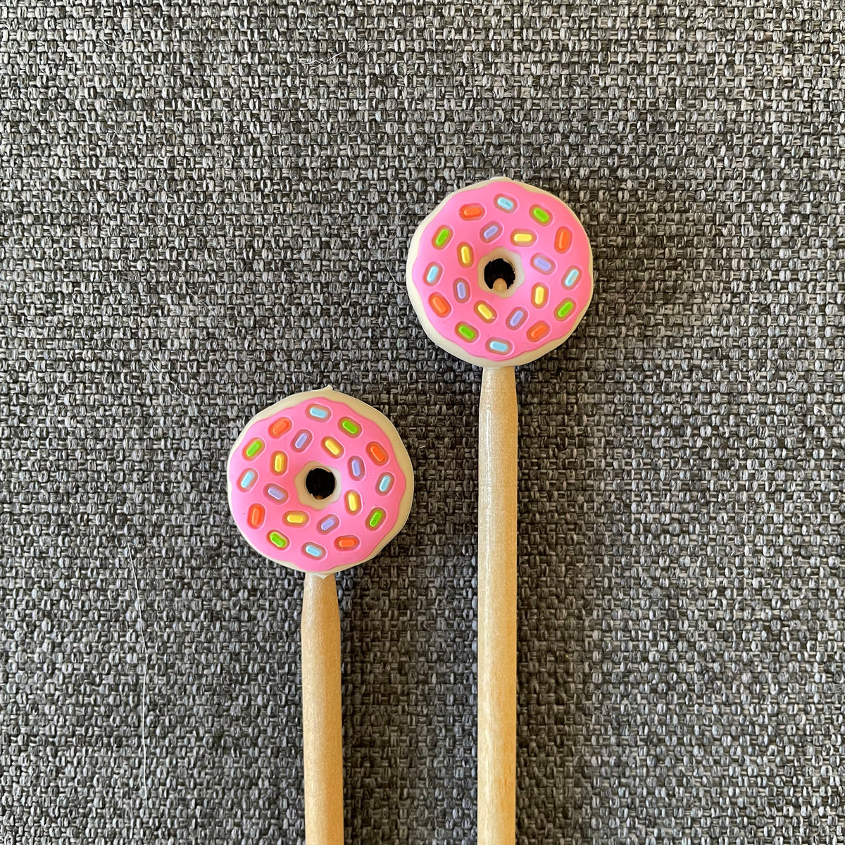 Two knitting needles topped with pink donut Stitch Stoppers