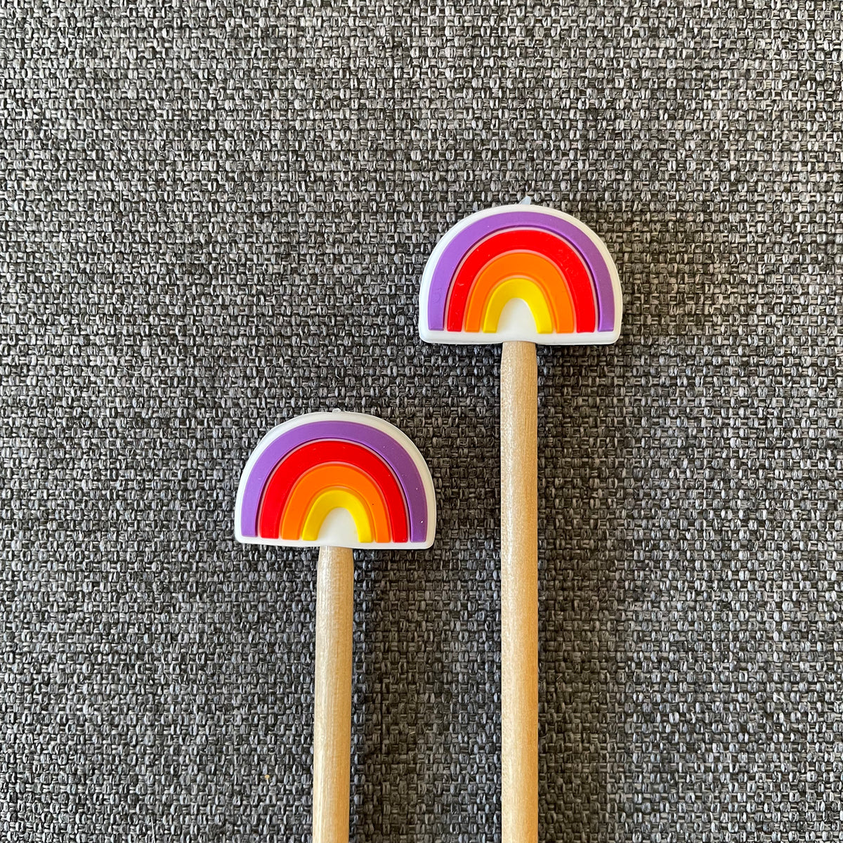 Two knitting needles topped with rainbow Stitch Stoppers
