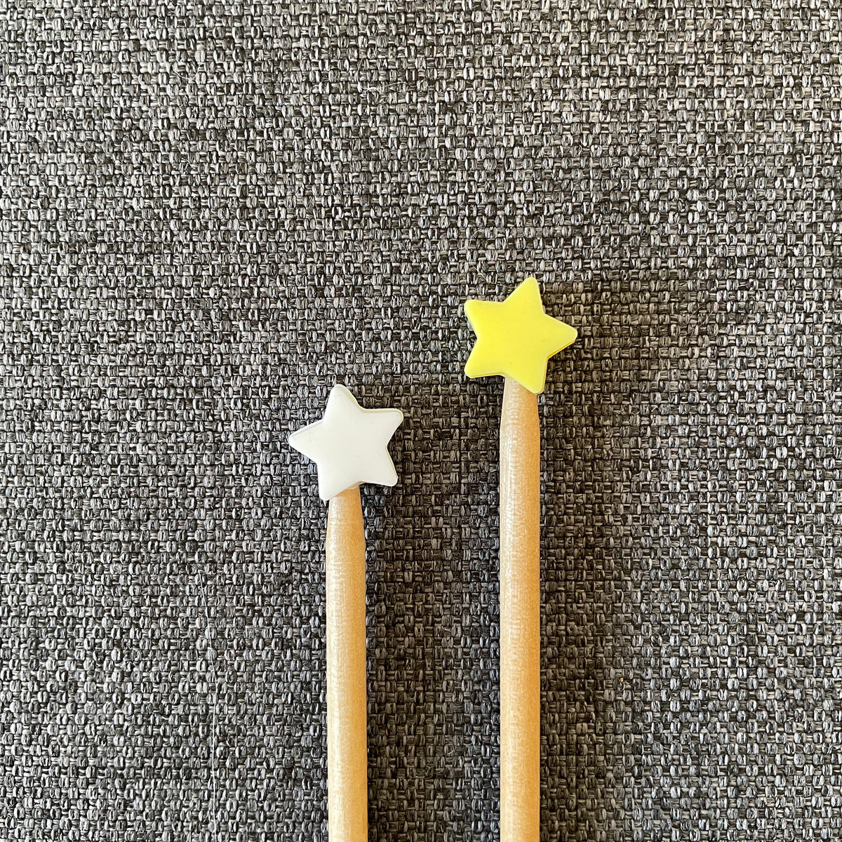 Two knitting needles topped with a white and a yellow star Stitch Stoppers